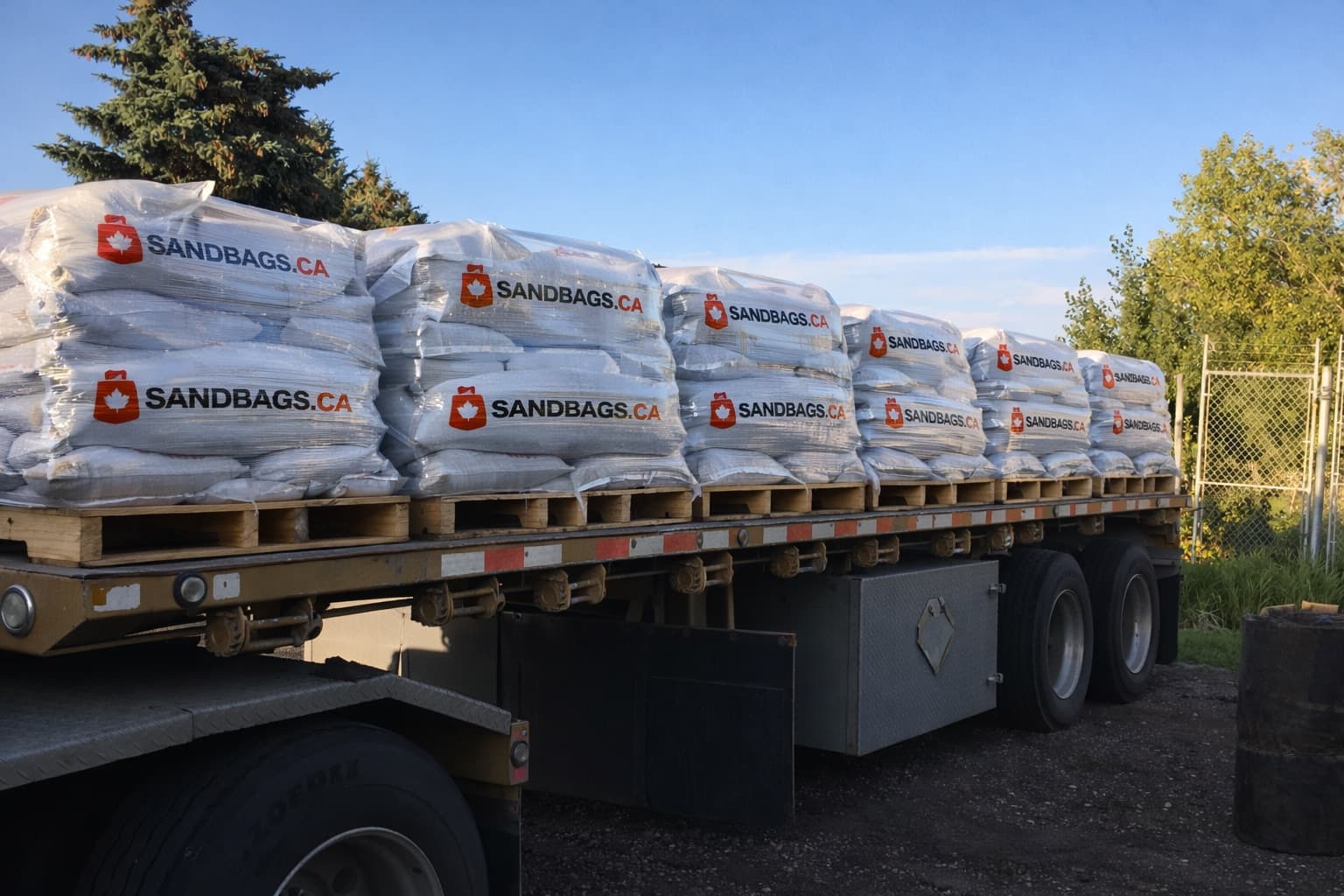 Flatbed trailer loaded with wrapped pallets of SandBags.ca sandbags