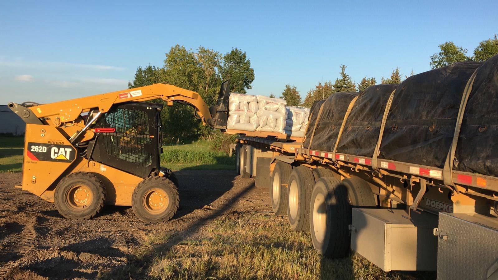 Skid steer loading pallets of sandbags onto a trailer